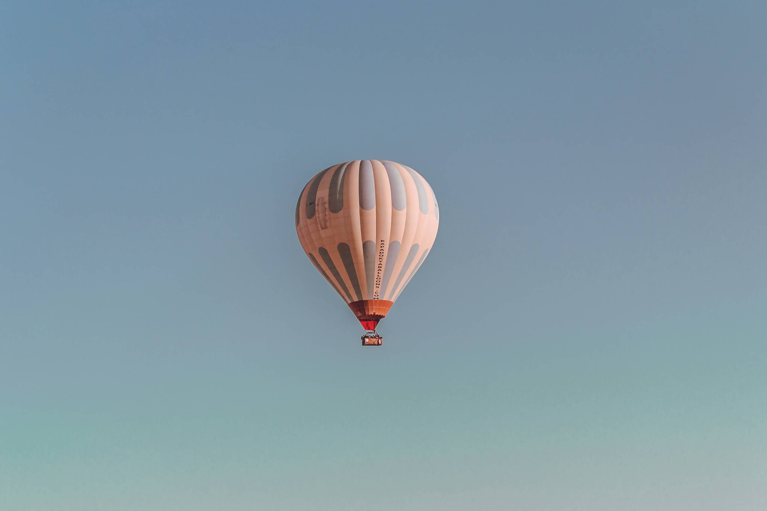 Apricot farbener Heißluftballon schwebt in einem blauen Himmel.